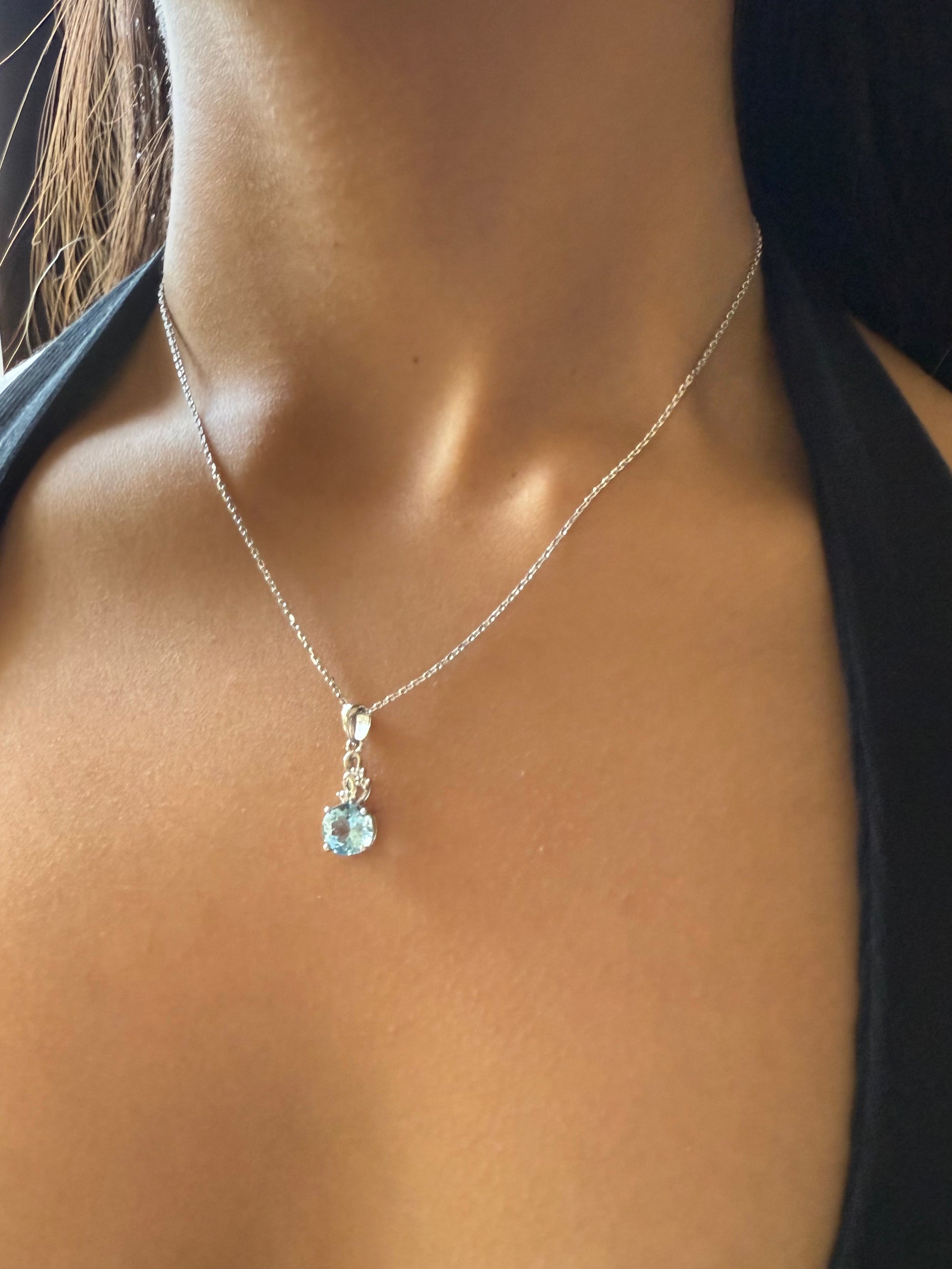 Necklace with a pendant featuring a blue gemstone on a person wearing a black top.