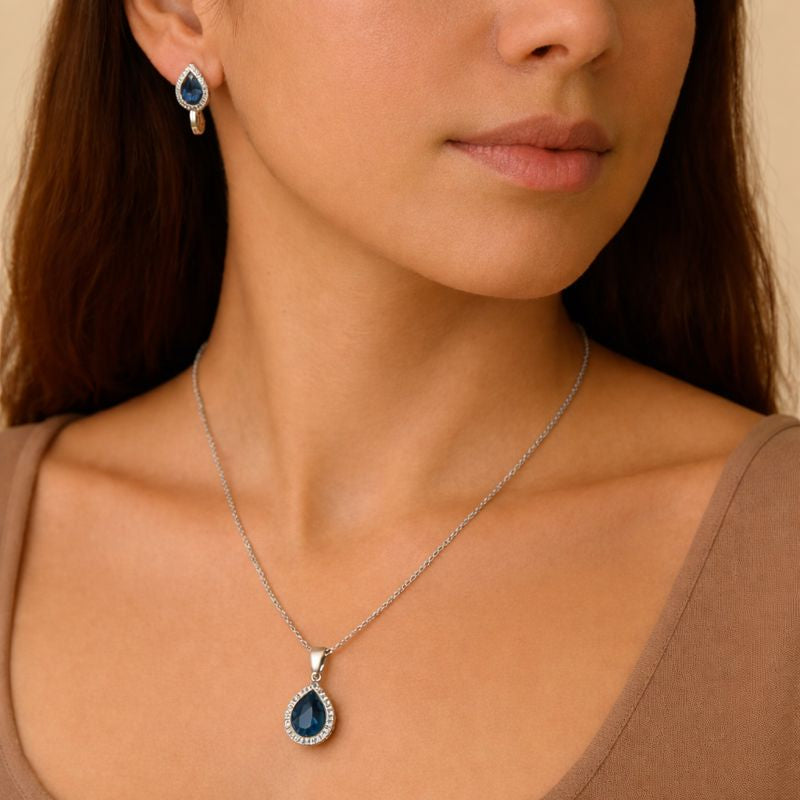 Woman wearing a silver necklace with a blue pendant and matching earrings.